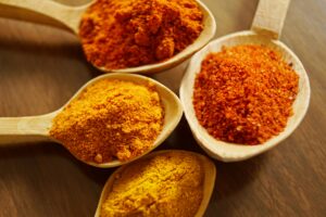 Close-up of vibrant spices like turmeric and chili powder in wooden spoons.